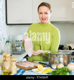 Souriante jeune femme au foyer cuisson de la soupe avec du poisson en filets à cuisine Banque D'Images