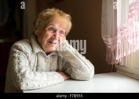 Femme âgée est assis à une table près de la fenêtre. Banque D'Images