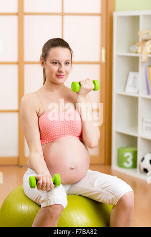 Femme enceinte de faire des exercices de conditionnement physique assis sur un ballon de gymnastique avec haltères Banque D'Images