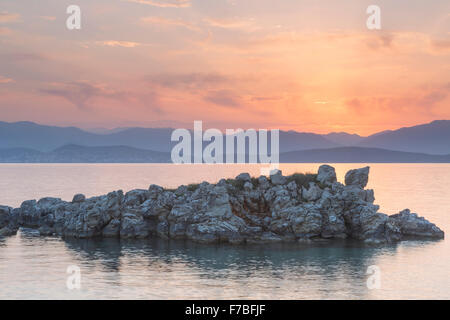 Les rochers s'élèvent de la mer Ionienne dans le Détroit de Corfou près de Kassiopi, Corfou. Le soleil se lève sur l'Albanie. Banque D'Images