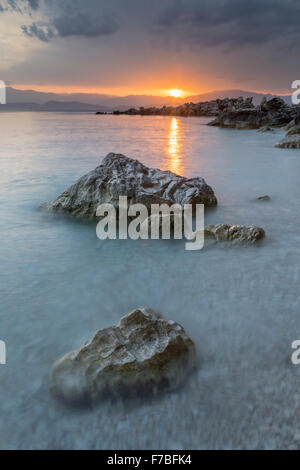 Les cailloux et les rochers sur la plage de Bataria, Kassiopi, Corfou sont éclairés avec la forte lumière orange de lever du soleil. Banque D'Images