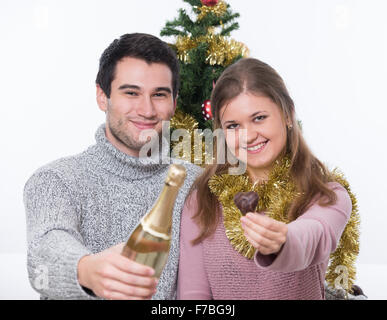 Jeune couple, homme et femme, assise en face d'arbre de Noël, la tenue de vin boutle Banque D'Images