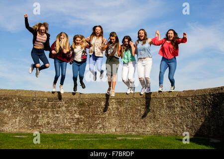 Huit adolescentes qui s'amusent à se tenir les mains et à sauter du mur du château Broughty Ferry lors d'une chaude journée ensoleillée à Dundee, au Royaume-Uni, Banque D'Images