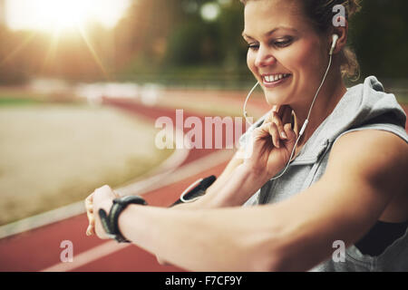 Close-up smiling sportswoman regardant sa montre et se sentir l'impulsion sur la voie avant la formation sur le terrain Banque D'Images