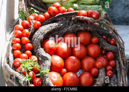 Panier en osier rustique rempli de tomates rouges disposés, les plus au centre, plus petites autour. Panier sur des marches en pierre. La lumière du soleil. Banque D'Images