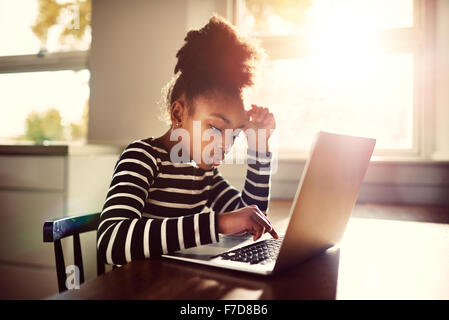 Jeune fille assise à la table à manger à la maison à travailler sur ses devoirs de l'école de taper une réponse sur un ordinateur portable, e- Banque D'Images