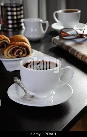 Tasse de café sur la table avec des petits pains et journaux Banque D'Images