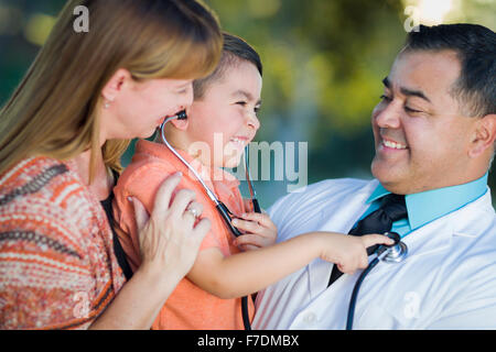 Happy Mixed Race Boy, de la mère et de l'Hispanic Doctor s'amusant avec stéthoscope à l'extérieur. Banque D'Images