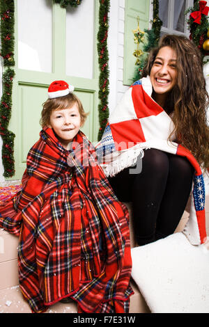 Famille heureuse à Noël de bonnets rouges en attente invités et souriant à l'extérieur chambre, frère et sœur hugging cheerful Banque D'Images