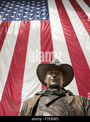 Santa Ana, Californie, USA. 27 Nov, 2015. Une plus grande que la vie statue en bronze de John Wayne est sur l'affichage à l'aéroport international John Wayne. Wayne, un acteur célèbre pour ses rôles de cow-boy, le vécu dans les environs de Newport Beach. La statue de bronze de Wayne est encadrée par un drapeau américain fond à partir derrière illustrant une image de patriotisme pour une génération qui a grandi sur ses films représentant l'individualisme farouche et emblématiques de l'époque beaucoup aimé dans l'histoire américaine et de la culture. Wayne est représenté, comme il l'a été dans la plupart de ses films de l'ouest, comme individualiste robuste, hea Banque D'Images