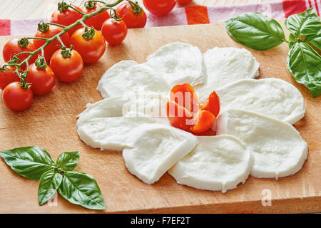 Tranches de mozzarella sur une planche à découper entouré par la tomate et basilic sur une table en bois Banque D'Images