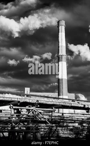 Immense cheminée d'usine en noir et blanc situé juste au-dessus vers un ciel bleu éructe des panaches de fumée ou la pollution en t Banque D'Images