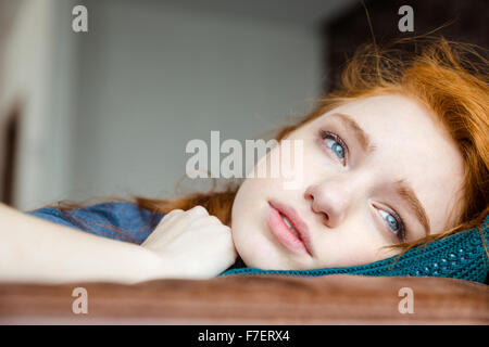 Pensive contrarié assez jeune femme aux cheveux rouges se trouvant sur l'oreiller en tricot Banque D'Images