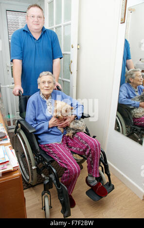 Carer mâle poussant une femme âgée en fauteuil roulant (pourrait être mère & fils) Banque D'Images