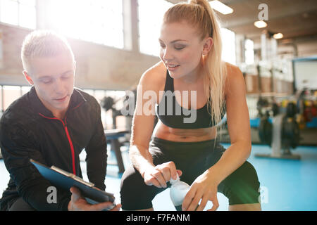 Vue d'un entraîneur personnel aider jeune femme avec son plan de remise en forme. Salle de fitness trainer et membre de discuter un plan d'entraînement sur clipboa Banque D'Images