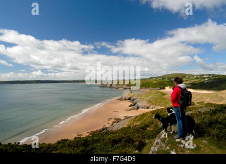 Femme et deux chiens donnant sur trois Rochers Baie, le Gower, dans le sud du Pays de Galles, Royaume-Uni Banque D'Images