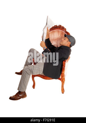 Un homme hispanique assis dans un fauteuil à lire son journal portant une casquette, isolée pour fond blanc. Banque D'Images
