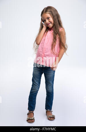 Full Length portrait of a happy little girl talking on the phone isolé sur fond blanc Banque D'Images