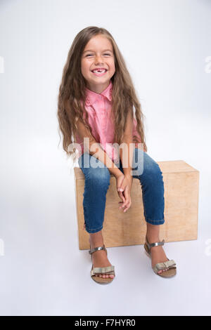 Portrait of a happy little girl sitting on wooden box isolé sur fond blanc Banque D'Images