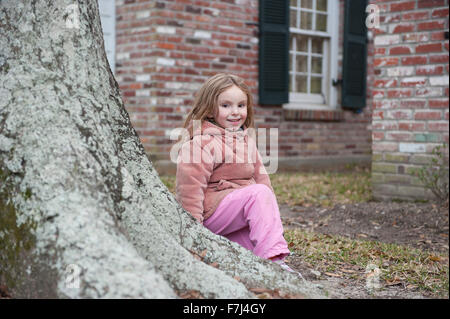 Petite fille assise à la base de l'arbre, smiling, portrait Banque D'Images