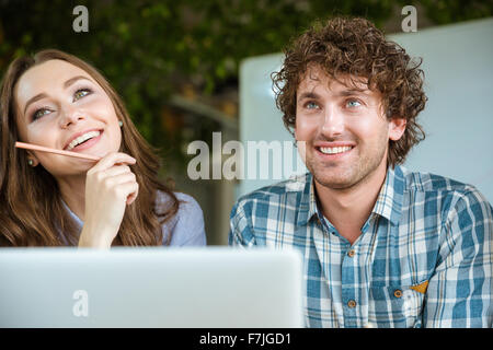 Belle jeune femme et beau jeune homme en chemise à carreaux using laptop and smiling Banque D'Images