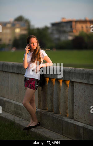 Adolescent Girl standing outdoors conversation sur le téléphone mobile pendant le coucher du soleil. Banque D'Images