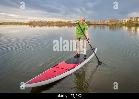 Senior male pagayeur sur un paddleboard, lac du Colorado avec un paysage d'automne et de sombres nuages Banque D'Images