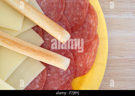 Haut de page fermer d'un papier jaune plaque avec des tranches de salami de Gênes et de fromage provolone gressins plus sur une table en bois Banque D'Images