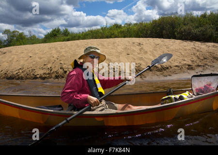 Man paddling un petit canot sur le lac Limekiln dans Old Forge, New York, avec une pagaie de kayak. Une plage de sable est à l'arrière. Banque D'Images