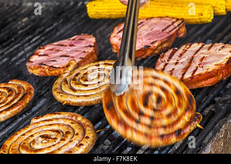 Des saucisses, du bacon et du maïs rôti sur le grill et retourné par Cook. Banque D'Images