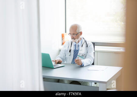 Un médecin travaillant à l'ordinateur portable au bureau du médecin Banque D'Images