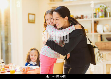 Travailler mother hugging daughter au revoir à table de petit déjeuner Banque D'Images