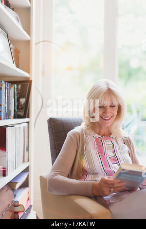 Smiling senior woman reading book in den Banque D'Images
