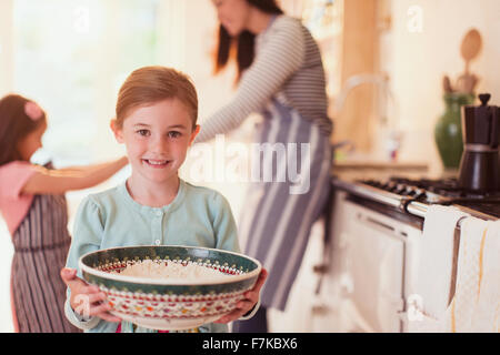 Portrait smiling girl holding bowl à pâte de farine dans la cuisine Banque D'Images