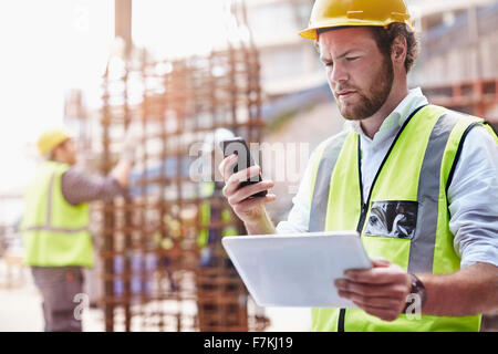 Construction Worker with digital tablet texting with cell phone at construction site Banque D'Images