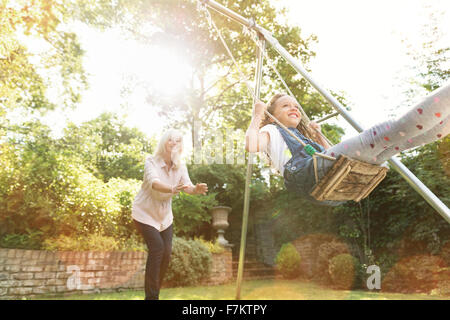 Grand-mère-fille poussant sur swing in backyard Banque D'Images