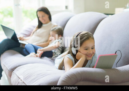 Fille avec écouteurs et tablette numérique portant sur le sofa du salon Banque D'Images