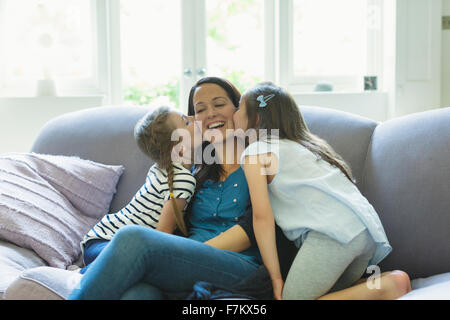 Filles embrassant les joues de la mère sur le sofa du salon Banque D'Images