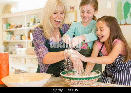 Grand-mère espiègle et petites-filles l'arrosage de la farine en cuisine Banque D'Images