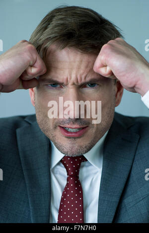 Businessman holding poings serrés contre la tête en colère, portrait Banque D'Images