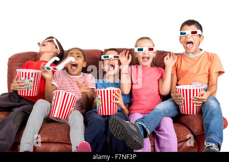 Groupe d'enfants avec des lunettes 3D et du pop-corn dans un canapé s'amusant Banque D'Images