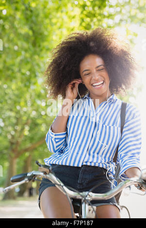 Femme enthousiaste avec afro équitation location listening to music on headphones Banque D'Images