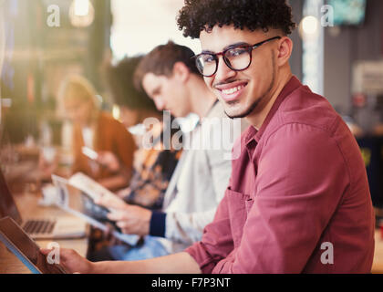 Portrait of smiling man avec les cheveux noirs bouclés using digital tablet in cafe Banque D'Images