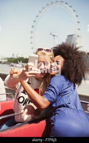 Amis enthousiastes en tenant sur selfies bus double étage avec London Eye en arrière-plan Banque D'Images