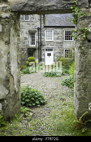 Cour pavée à côté de la maison de Plas yn, * Plusieurs autres calvaires parsèment Gwynedd. Il est plein d'auto-ensemencement de géraniums et de fougères autour de buis taillés topiary. Banque D'Images