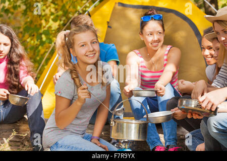 Smiling girl cuisiniers soupe dans pot près de la tente jaune Banque D'Images