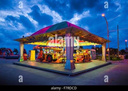 Parc d'enfants de nuit, vue d'un enfant lumineux's ride se détachant sur de sombres nuages au-dessus de la zone portuaire à Marsala, en Sicile. Banque D'Images