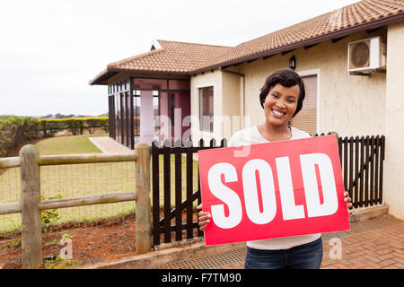 Happy African woman holding sold sign in front of house Banque D'Images