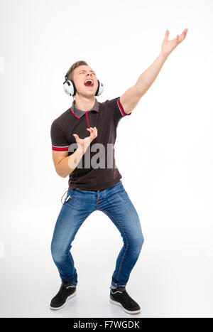 Beau jeune homme espiègle en noir T-shirt et jeans écouter de la musique avec un casque, chantant et dansant sur white backg Banque D'Images