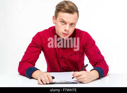 Curieux suspectes young male en chemise rouge avec Raised Eyebrow writing on clipboard sur fond blanc Banque D'Images